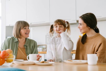 Téléchargez les photos : Famille blanche riant et prenant le petit déjeuner tout en passant du temps ensemble à la maison - en image libre de droit