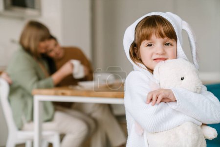 Téléchargez les photos : Blanc fille souriant et tenant jouet tout en passant du temps avec sa famille à la maison - en image libre de droit