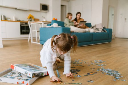 Téléchargez les photos : Blanc fille blonde compléter puzzle tout en passant du temps avec sa famille à la maison - en image libre de droit