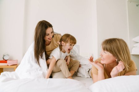 Photo for White girl playing with her mother and granddaughter in bed at home - Royalty Free Image