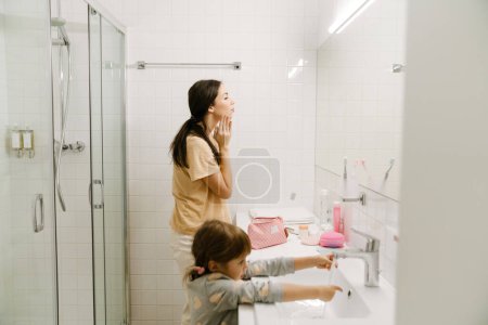 Téléchargez les photos : Femme blanche et sa fille se lavent ensemble dans la salle de bain à la maison - en image libre de droit