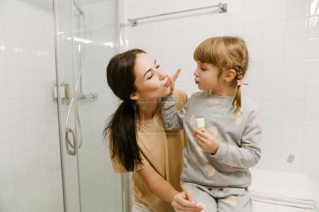 Téléchargez les photos : Femme blanche souriant tout en faisant du maquillage ensemble dans la salle de bain à la maison - en image libre de droit
