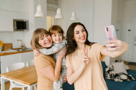 Photo for White family gesturing while taking selfie photo on mobile phone at home - Royalty Free Image