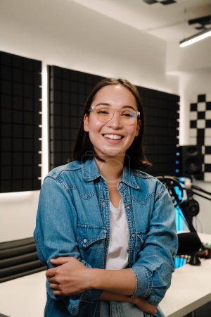 Photo for Beautiful happy young female radio host smiling while broadcasting in studio - Royalty Free Image
