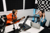 Young white man playing guitar while happy woman recording podcast on laptop in radio studio Poster #626682910