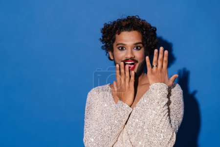 Photo for Young excited man with makeup expressing surprise at camera isolated over blue background - Royalty Free Image