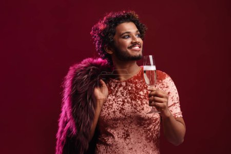 Photo for Young man with fur jacket drinking champagne and smiling isolated over red background - Royalty Free Image