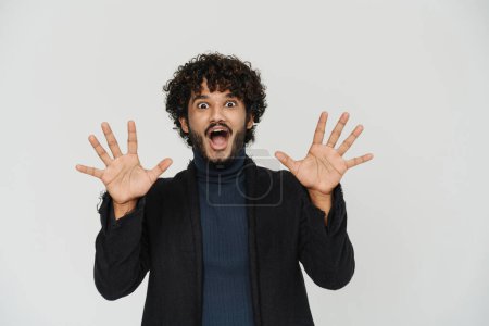Photo for Young handsome curly indian man in black coat with raised hands and splayed fingers over isolated grey background - Royalty Free Image