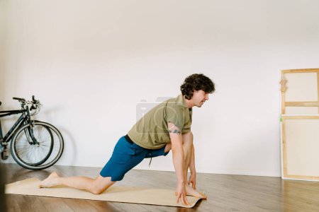 Foto de Hombre blanco usando pantalones cortos haciendo ejercicio durante la práctica de yoga en casa - Imagen libre de derechos