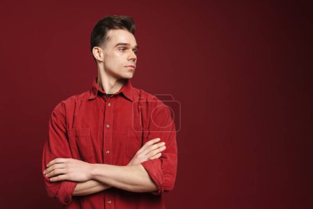 Foto de Joven hombre blanco con camisa posando y mirando a un lado aislado sobre fondo rojo - Imagen libre de derechos