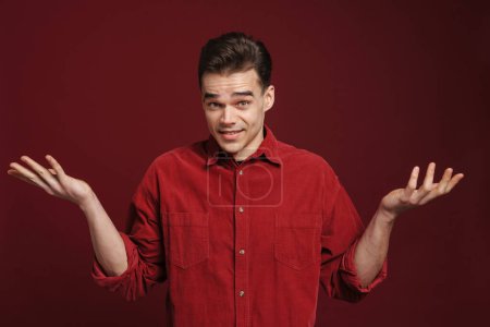 Photo for Young perplexed man wearing shirt looking and gesturing at camera isolated over red background - Royalty Free Image