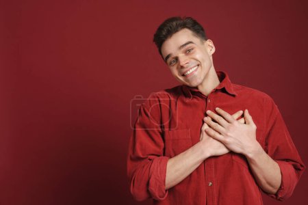 Photo for Young white man smiling and holding hands on his chest isolated over red background - Royalty Free Image