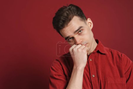 Photo for Young sad man propping up his head and looking at camera isolated over red background - Royalty Free Image