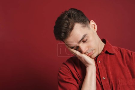 Téléchargez les photos : Jeune homme fatigué soutenant sa tête et glissant isolé sur fond rouge - en image libre de droit