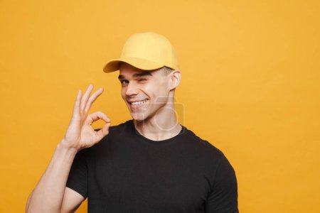 Téléchargez les photos : Jeune homme blanc portant chapeau clin d'oeil et montrant ok signe isolé sur fond jaune - en image libre de droit