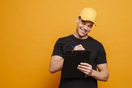 Photo for Young white man smiling while writing on clipboard isolated over yellow background - Royalty Free Image
