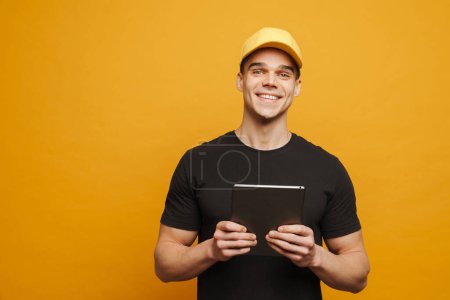 Téléchargez les photos : Jeune homme blanc portant un bonnet souriant tout en utilisant un ordinateur tablette isolé sur fond jaune - en image libre de droit