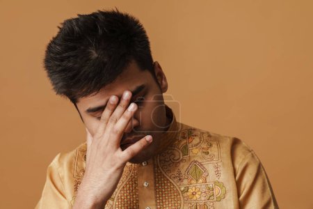 Téléchargez les photos : Jeune homme indien brune couvrant son visage avec la main isolé sur fond jaune - en image libre de droit