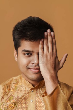 Téléchargez les photos : Jeune homme indien brune souriant et couvrant son visage avec la main isolée sur fond jaune - en image libre de droit