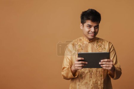 Foto de Joven morena indio hombre sonriendo y sosteniendo tableta aislado sobre fondo amarillo - Imagen libre de derechos