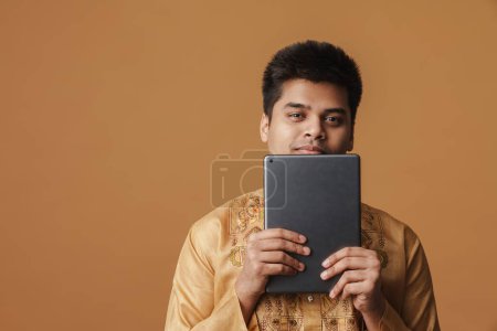 Foto de Joven morena indio hombre sonriendo y sosteniendo tableta aislado sobre fondo amarillo - Imagen libre de derechos