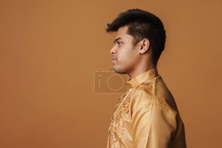 Téléchargez les photos : Jeune homme indien brune en chemise traditionnelle debout de profil isolé sur fond jaune - en image libre de droit