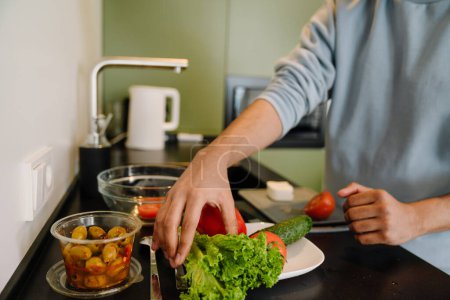 Téléchargez les photos : Main masculine prenant des légumes pour cuisiner la salade dans une cuisine confortable à la maison gros plan - en image libre de droit