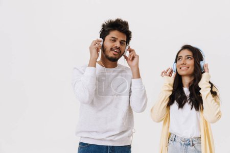 Foto de Joven pareja india escuchando música con auriculares y teléfonos celulares aislados sobre fondo blanco - Imagen libre de derechos