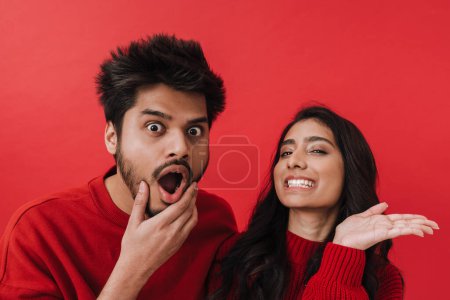 Foto de Joven pareja india expresando sorpresa mientras posan juntos aislados sobre fondo rojo - Imagen libre de derechos