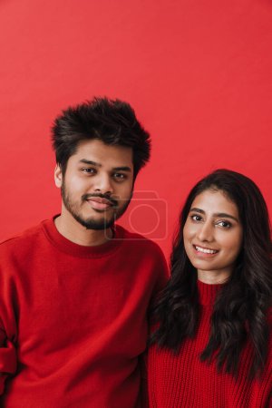 Téléchargez les photos : Jeune couple indien riant tout en posant ensemble isolé sur fond rouge - en image libre de droit