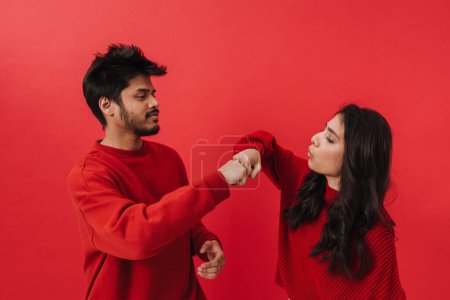 Foto de Joven pareja india riendo y golpeando sus puños mientras posan juntos aislados sobre fondo rojo - Imagen libre de derechos