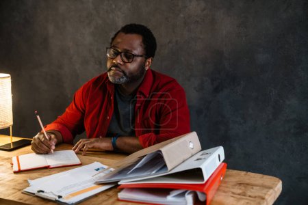 Téléchargez les photos : Homme barbu noir dans des lunettes de vue note tout en travaillant dans le bureau - en image libre de droit