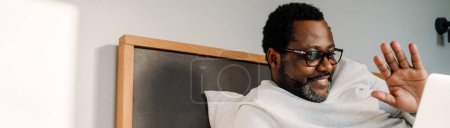 Foto de Hombre afroamericano maduro usando anteojos usando laptop mientras descansa en casa - Imagen libre de derechos