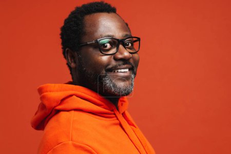 Téléchargez les photos : Homme afro-américain adulte portant des lunettes souriant à la caméra isolée sur fond orange - en image libre de droit