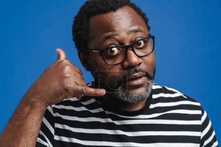 Téléchargez les photos : Homme afro-américain adulte portant des lunettes signe d'appel gestuel à la caméra isolé sur fond bleu - en image libre de droit