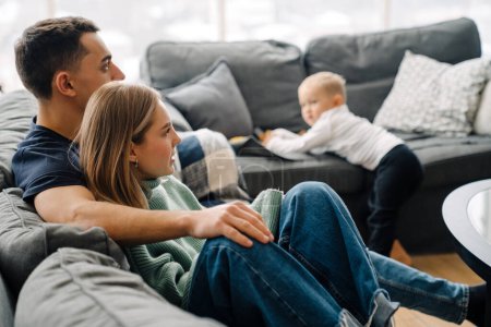 Foto de Joven hombre blanco y mujer con hijo pequeño sentado en el sofá y viendo la televisión en casa - Imagen libre de derechos