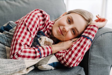 Photo for Young white woman wearing pajama smiling while lying on sofa at home in morning - Royalty Free Image