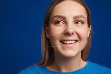 Photo for Portrait of young beautiful happy smiling girl looking leftward over blue isolated background - Royalty Free Image