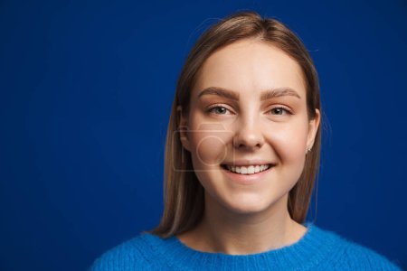 Téléchargez les photos : Portrait de jeune belle fille souriante heureuse regardant à la caméra sur fond bleu isolé - en image libre de droit