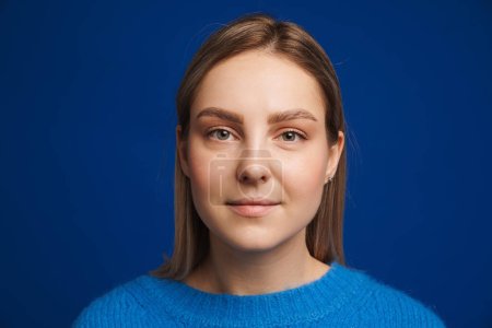 Photo for Portrait of young beautiful calm girl looking in camera over blue isolated background - Royalty Free Image