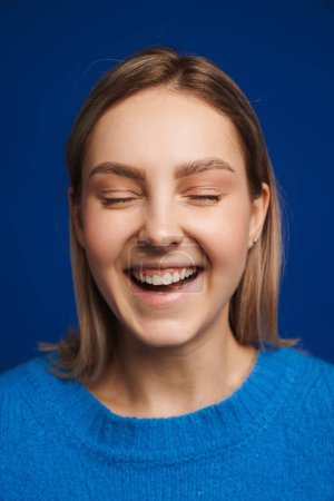 Foto de Retrato de joven hermosa chica sonriente feliz con los ojos cerrados sobre fondo azul aislado - Imagen libre de derechos