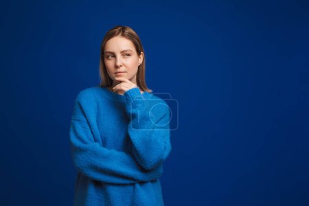 Photo for Young thoughtful beautiful girl touching chin and pondering looking rightward over blue isolated background - Royalty Free Image
