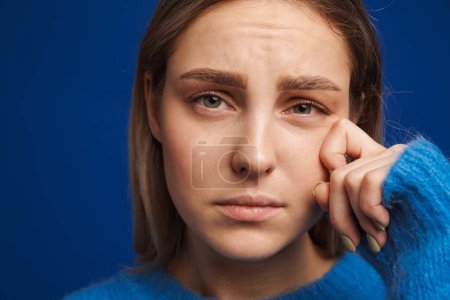 Foto de Mujer joven limpiando sus lágrimas mientras llora sobre fondo azul aislado - Imagen libre de derechos