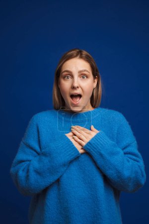 Photo for Young white excited woman wearing sweater keeping hands on her chest standing isolated over blue background - Royalty Free Image