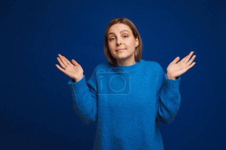 Foto de Joven hermosa chica en suéter azul mostrando no sé gesto sobre fondo azul aislado - Imagen libre de derechos