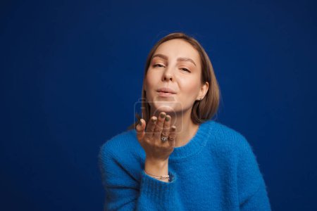 Photo for Young white happy woman wearing sweater blowing air kiss at camera standing isolated over blue background - Royalty Free Image