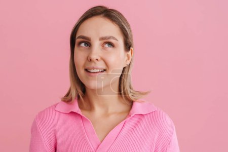 Téléchargez les photos : Jeune belle femme blanche portant chemise souriante et regardant vers le haut debout isolé sur fond rose - en image libre de droit