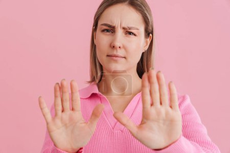 Téléchargez les photos : Jeune femme blanche contrariée portant chemise fronçant les sourcils et faisant un geste d'arrêt debout isolé sur fond rose - en image libre de droit