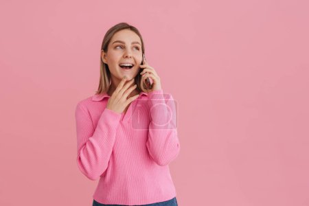Foto de Joven linda chica hablando por teléfono en suéter rosa de pie sobre el fondo rosa aislado - Imagen libre de derechos