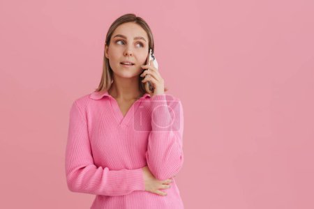 Photo for Young cute girl talking on the phone in pink sweater standing over isolated pink background - Royalty Free Image